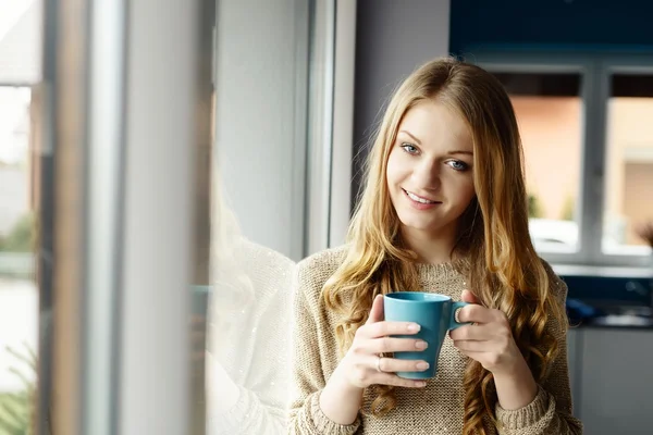 Linda mulher loira sorrindo bebendo café pela janela — Fotografia de Stock
