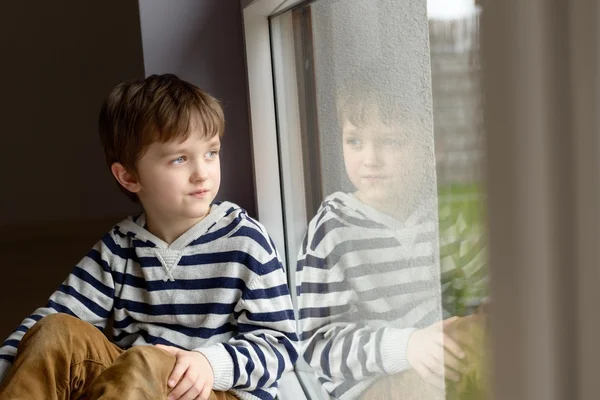 Задумчивый маленький мальчик сидит у окна — стоковое фото