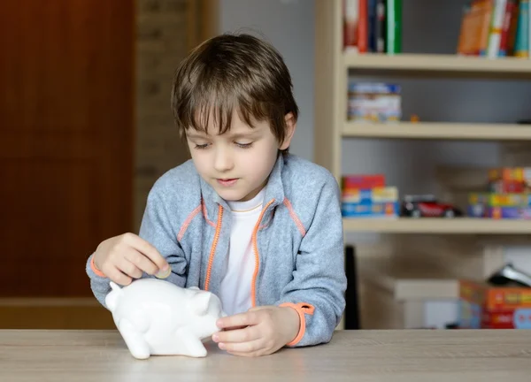 Little boy putting his saving to his piggy bank — Stock Photo, Image