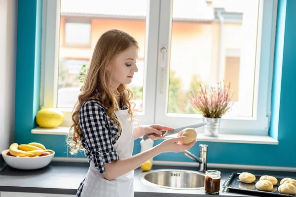 Frau schneidet in Küche mit Messer ein Brötchen. — Stockfoto