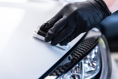 Seramik kaplamanın yakın çekimi, farların yanındaki araba gövdesi paneline elle uygulanıyor, kesin teknik, boya koruması ve profesyonel araba temizleme servisi gösteriyor..