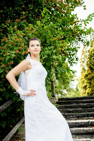Beautiful stylish brunette bride posing on the stairs in the park — Stock Photo, Image