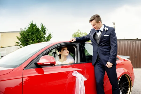 Young bride sits behind the wheel of a red sports car — Stock Photo, Image