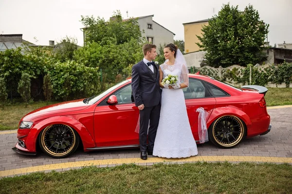 Jovem casal em pé na frente de um carro vermelho e olhando um para o outro — Fotografia de Stock