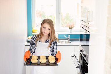 Blond woman holding a baking tray with freshly baked bread rolls.  clipart