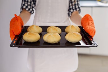 woman holding a baking tray with freshly baked bread rolls.  clipart