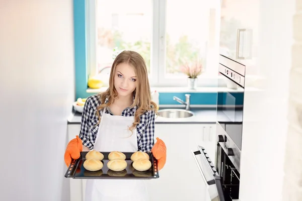 Mujer rubia sosteniendo una bandeja para hornear con panecillos recién horneados . — Foto de Stock