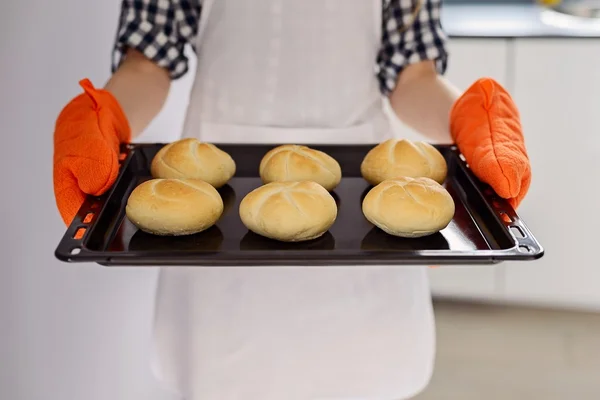 Frau hält Backblech mit frisch gebackenen Semmeln in der Hand. — Stockfoto