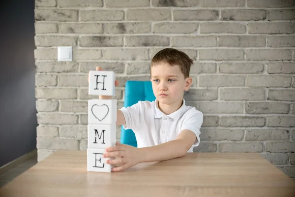 Liten pojke leker med kuber och sätter det tillsammans i ordet "hem" — Stockfoto