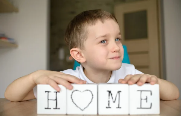 Niño feliz juega con cubos y lo pone juntos en la palabra "casa ". —  Fotos de Stock