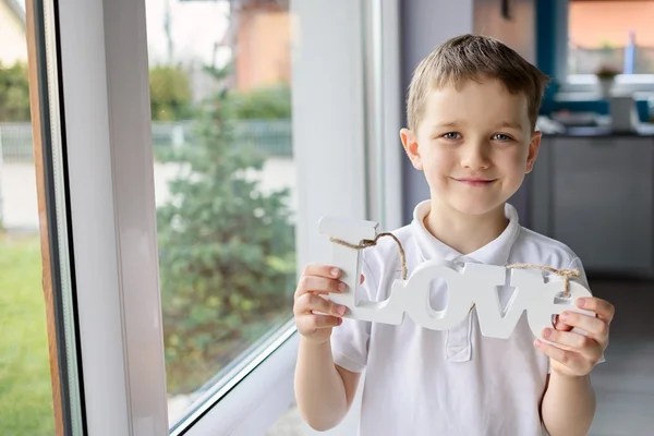 Glad liten pojke håller en trä inskrift med ordet "love" — Stockfoto