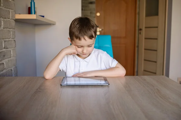 Little 6 year old boy using tablet while sitting at the table. — Stock Photo, Image