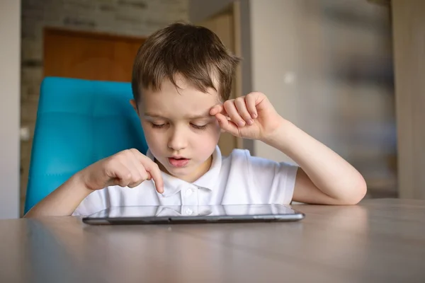6-летний ребенок, сидя за столом, пользуется планшетом — стоковое фото