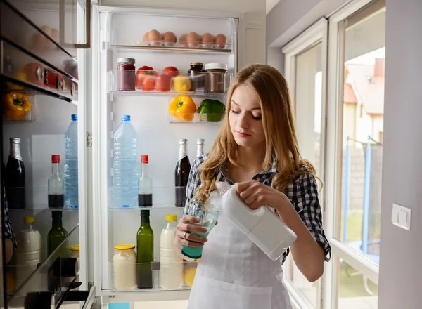Mujer vertiendo leche mientras está de pie cerca del refrigerador — Foto de Stock