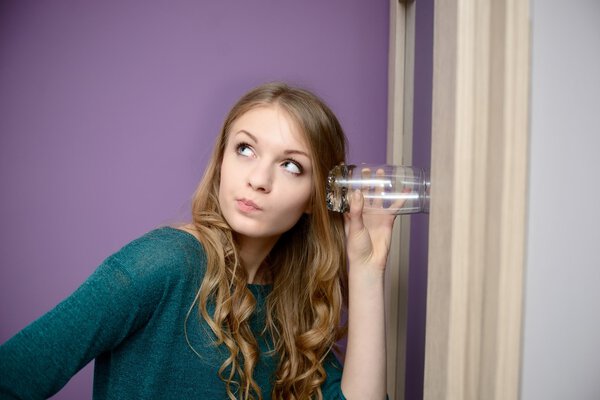 Young blonde woman listening in to a conversation with a glass