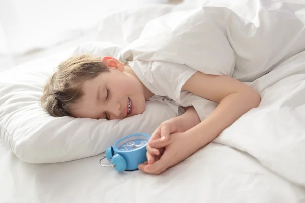 Feliz sorrindo menino adormecido com despertador perto de sua cabeça — Fotografia de Stock