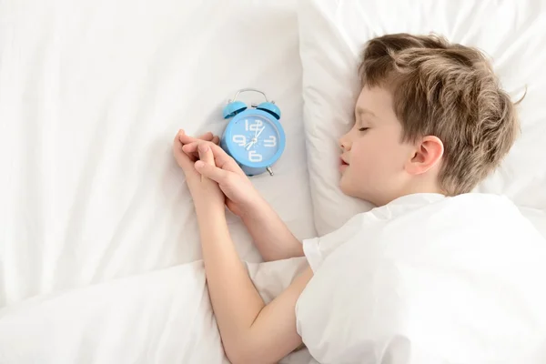 Vista superior do menino dormindo na cama branca com despertador perto de sua cabeça . — Fotografia de Stock