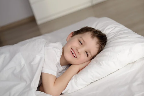 Kleiner Junge wacht mit offenen Augen im weißen Bett auf — Stockfoto