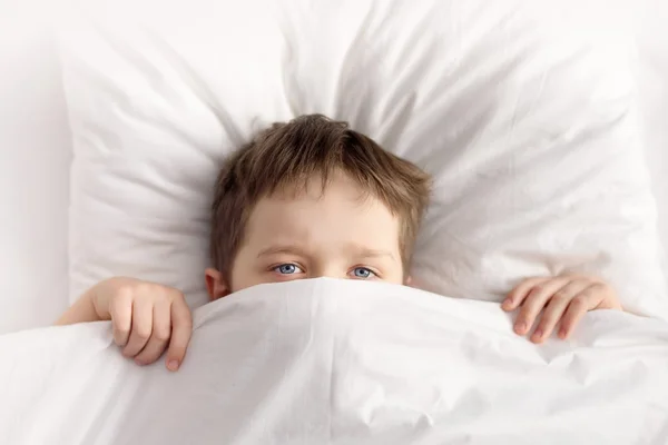 Μικρό αγόρι που κρύβεται στο κρεβάτι κάτω από την κουβέρτα στο σπίτι — Φωτογραφία Αρχείου