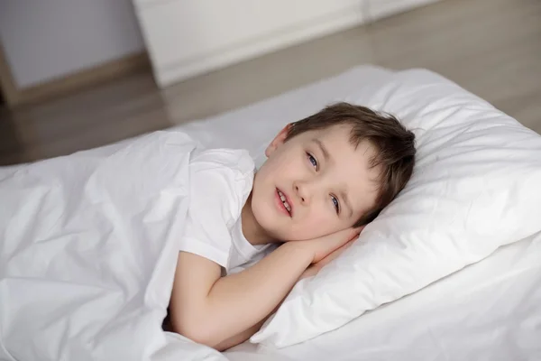 Kisfiú abban rejlik, hogy nyitott szemmel fehér ágy — Stock Fotó
