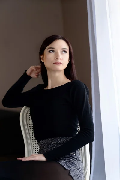 Junge Frau sitzt auf dem altmodischen Stuhl am Fenster. — Stockfoto