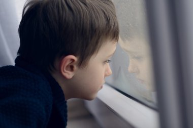 Küçük çocuk Dur yağmur için pencere tarafından bekleyen.