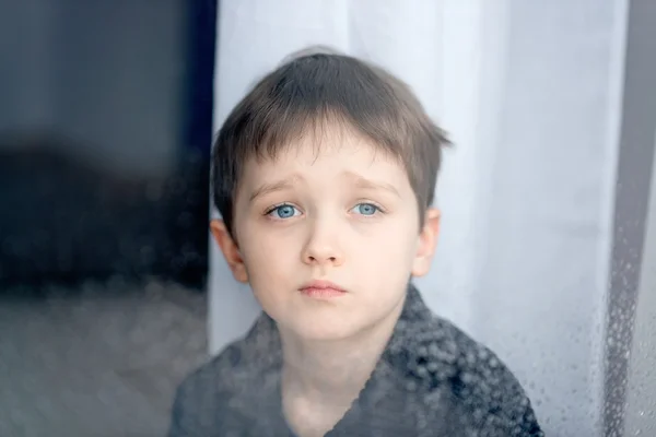 Depressed 7 years boy child looking out the window. — Stock Photo, Image