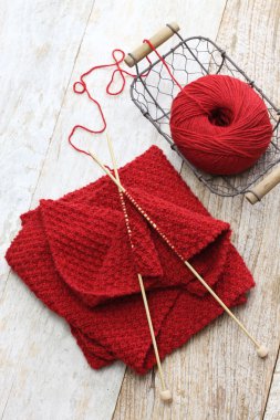 Kırmızı eşarp, iplik topu ve örgü iğneleri örme el