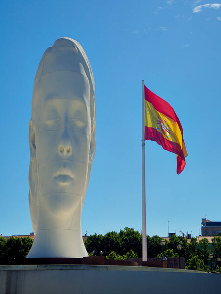 Madrid, Spain - July 12, 2021. Julia, a sculpture by Jaume Plensa with the Spanish flag in the background. Plaza de Colon square. Madrid, Spain.