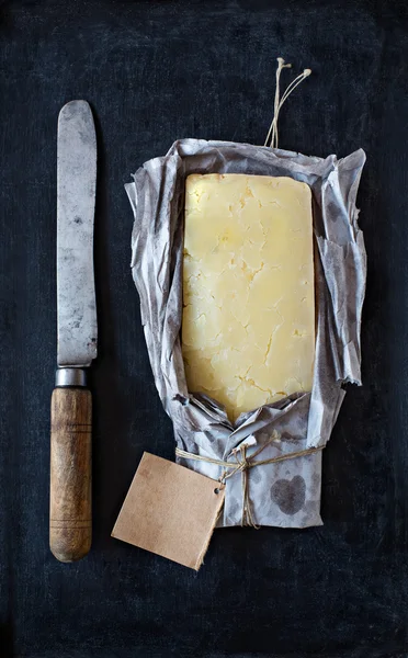 Ώριμη cheddar τυρί τυλιγμένα σε ρουστίκ χαρτί και ένα vintage μαχαίρι. — Φωτογραφία Αρχείου