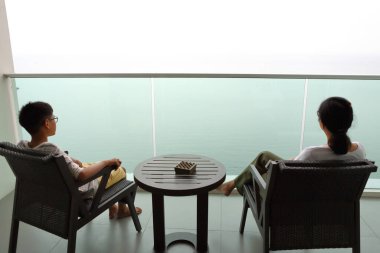Anne ve oğlu balkon sandalyelerinde oturup deniz manzarasına bakıyorlar.