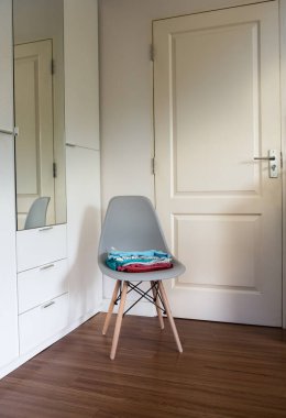 Modern sandalyede, yatak odasındaki dolabın yanında güneş ışınlarıyla katlanmış temiz giysiler yığını..