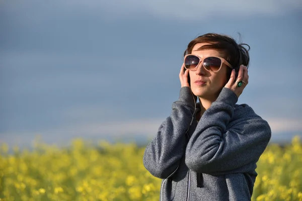 Mujer joven con gafas de sol escuchando música en auriculares — Foto de Stock