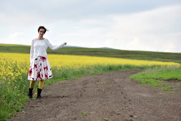 Сексуальная молодая женщина в платье, путешествующая автостопом возле поля на каноле — стоковое фото