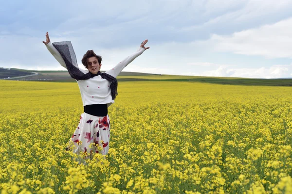 Mujer feliz saltando en medio de un campo de canola — Foto de Stock