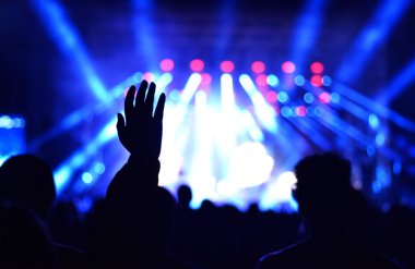 Parlak sahne ışıkları önünde konser kalabalığının silueti.