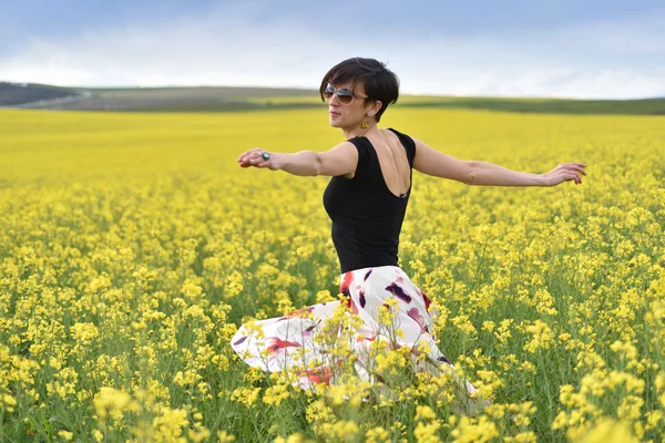 Hermosa mujer animando en campo de colza y disfrutando soleado su —  Fotos de Stock