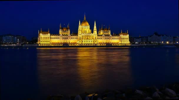 时间流逝的布达佩斯国民议会在夜间照明。多瑙河在帆船与前景 — 图库视频影像