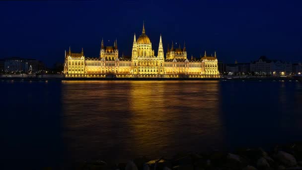 时间流逝的布达佩斯国民议会在夜间照明。多瑙河在帆船与前景 — 图库视频影像