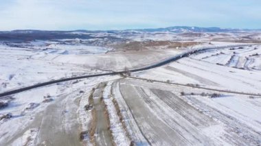 Soğuk kış güneşli bir günde insansız hava aracıyla araba süren dolambaçlı bir yolun havadan görünüşü.