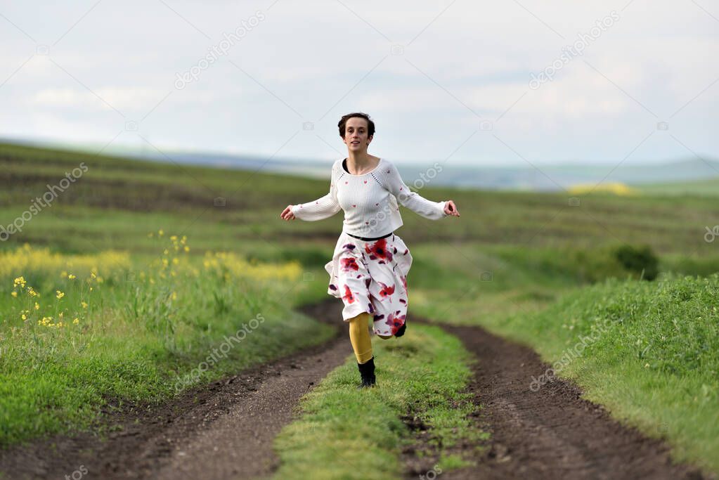 Joyful young woman in skirt running in canola field in the spring