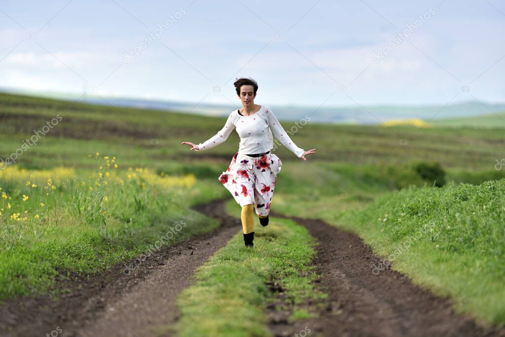 Joyful young woman in skirt running in canola field in the spring