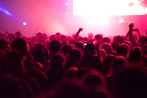 Unidentified crowd of people in red stage lights partying at a live concert at music festival