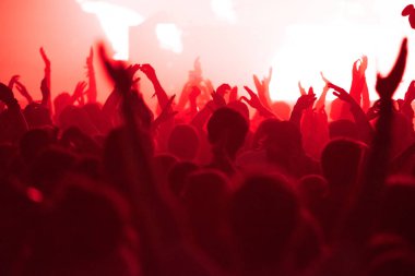 Konser kalabalığı alkışlıyor ve kırmızı sahne ışıkları altında parti veriyor.