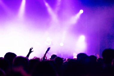 Konserde kollarını açarak kalabalığın dikey görüntüsü. Arka planda parlak sahne ışıkları