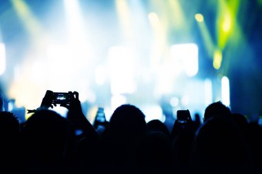 Ellerin silueti akıllı telefonlarla bir konser kaydediyor. Konseri fotoğraflamak için akıllı telefon kullanan bir sürü insan var.