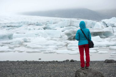 İzlanda 'daki Vatnajokull Ulusal Parkı' ndaki Fjallsarlon Buzul Gölü 'nde yüzen buzdağlarına hayran olan bir turist. Küresel ısınma, iklim değişikliği kavramı