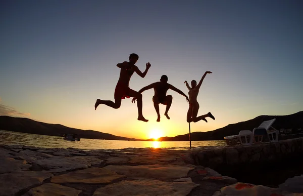 Sylwetka przyjaciół skoki na zachód słońca na plaży — Zdjęcie stockowe
