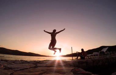 Kız gün batımında sahilde atlama