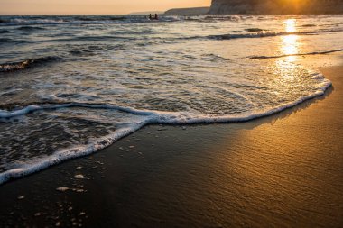 Kumlu plaj altın günbatımı sırasında yaklaşan dalgalar